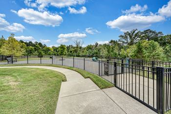 A park with a black fence and a sidewalk and grass